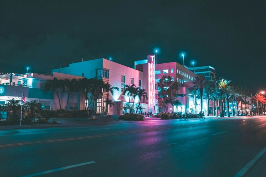 A hotel with a neon sign reading TROPICS on a palm-lined street at night